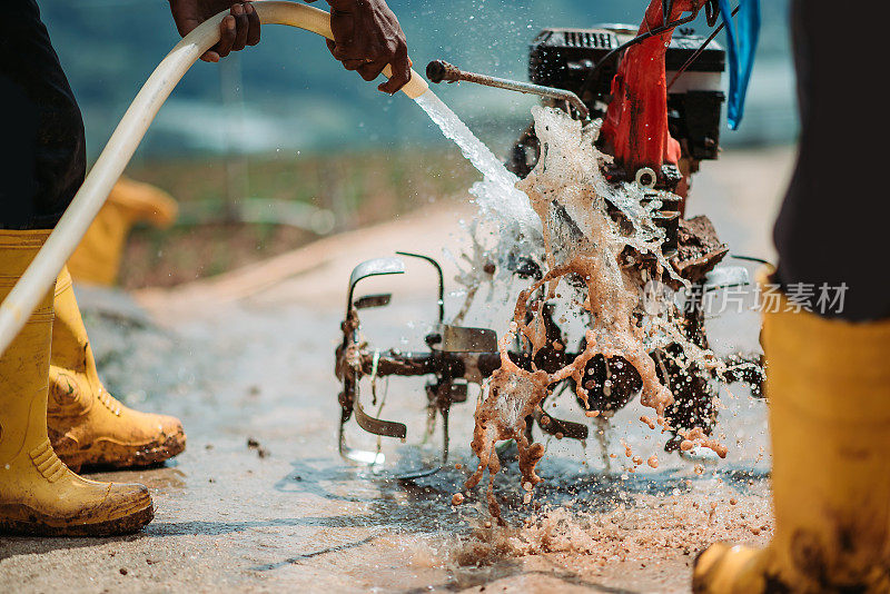 亚洲男性农民用水管清洁手扶拖拉机
