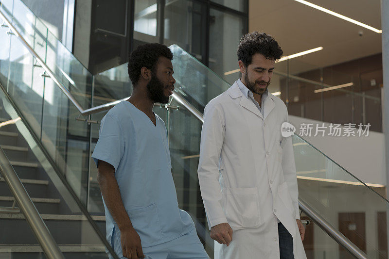 医生和黑人男护士一边走下医院的楼梯一边交谈。