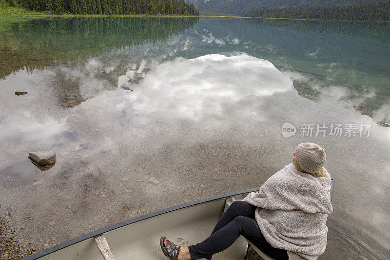 一个裹着毯子的女人坐在高山湖上的小船上