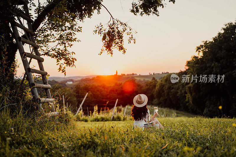 葡萄园里的女人看着夕阳，享受着美酒。