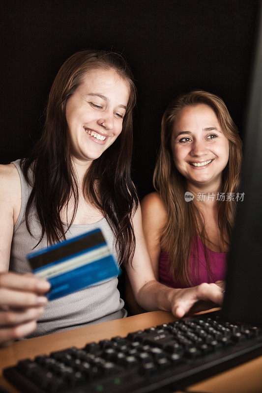 两个年轻的女人开心地微笑着用信用卡在网上购物