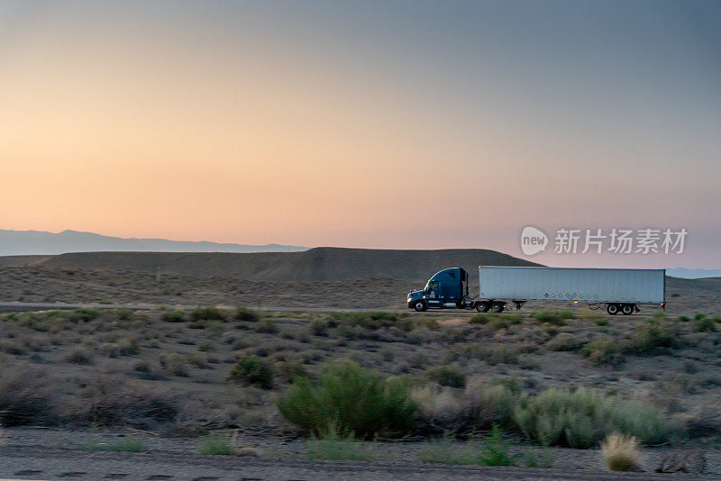 一辆商业货运半挂车在高速公路上向东行驶，一个戏剧性的日落背景