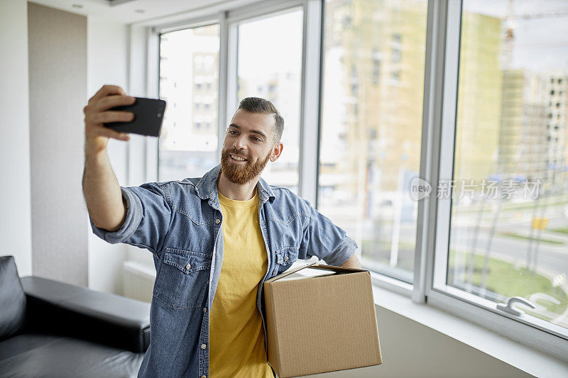 一个男人拿着一个纸箱，在他的新公寓里自拍