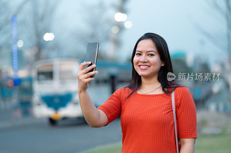 一名年轻女子在城市公园用手机自拍。