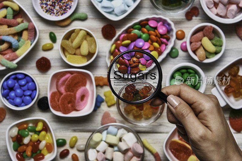 含糖食品的营养成分。俯视图的彩色软糖，棒棒糖，糖果和棉花糖与一个放大镜