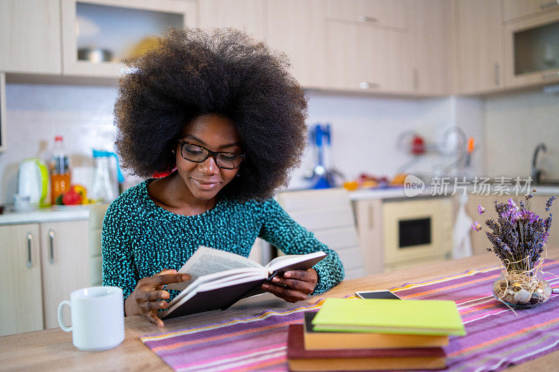 年轻女子坐在厨房的桌子上看书