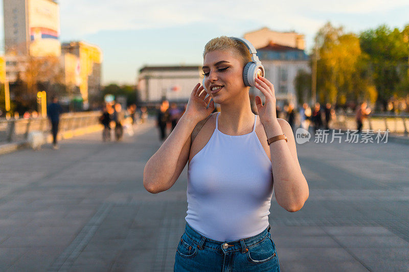 美丽的年轻女子，金色短发，一边听音乐，一边穿过城市