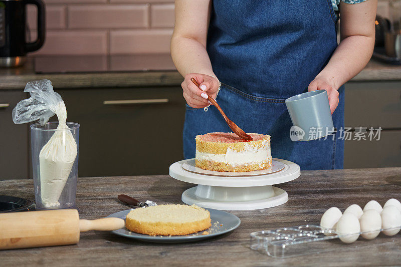 女性的手用木勺在圆饼上为饼层喷洒孕液。烹饪自制的蛋糕。家里的蛋糕