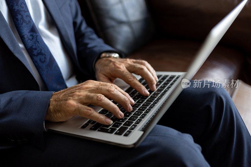 一个高级商人在笔记本电脑键盘上打字的特写