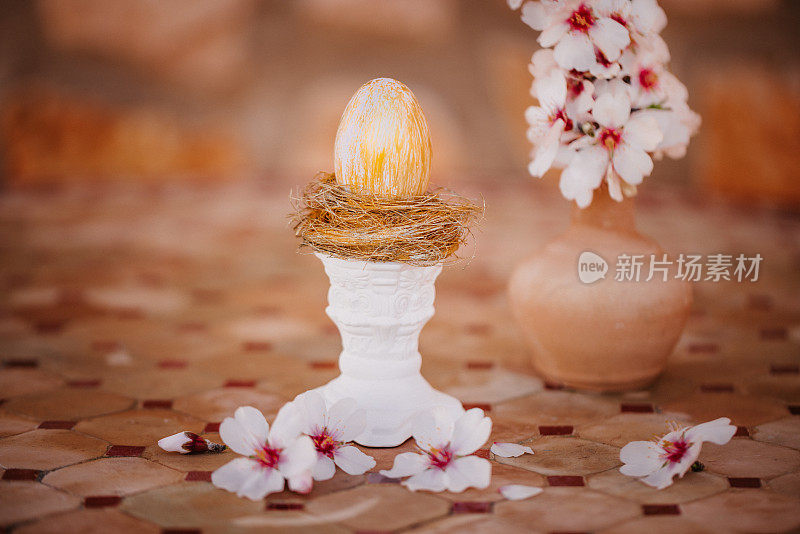 金色的复活节彩蛋在一个金色的巢上，在一个白色的柱子上的老桌子上，杏仁花
