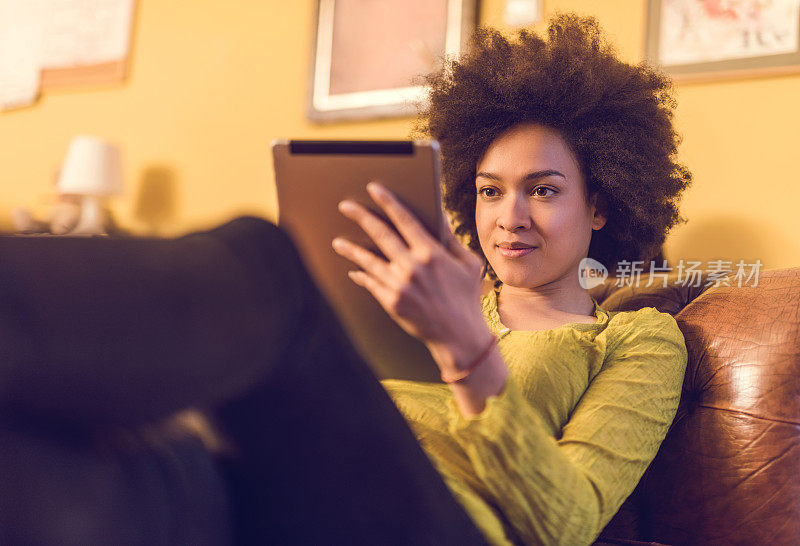 一名非裔美国妇女在家享受和使用数字平板电脑。