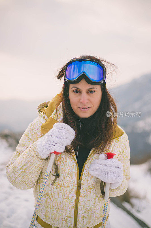 近景美丽的年轻女子在冬天的衣服站在一边，手拿木棍的背景雪山