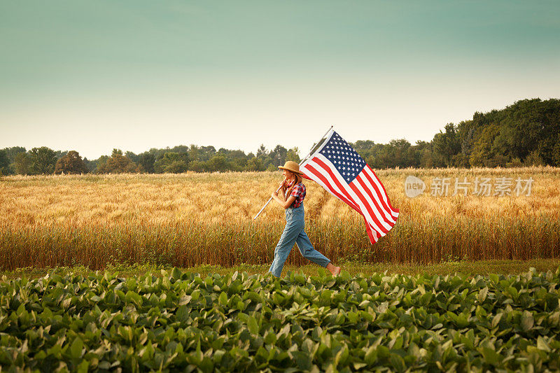 农民女孩挥舞着美国国旗穿过夏天的农田