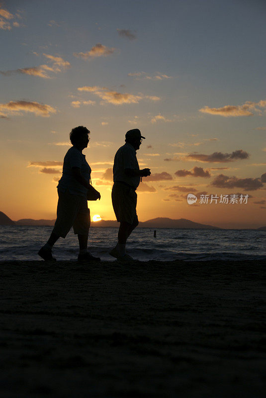 老年夫妇的剪影走过金色的热带日落海滩