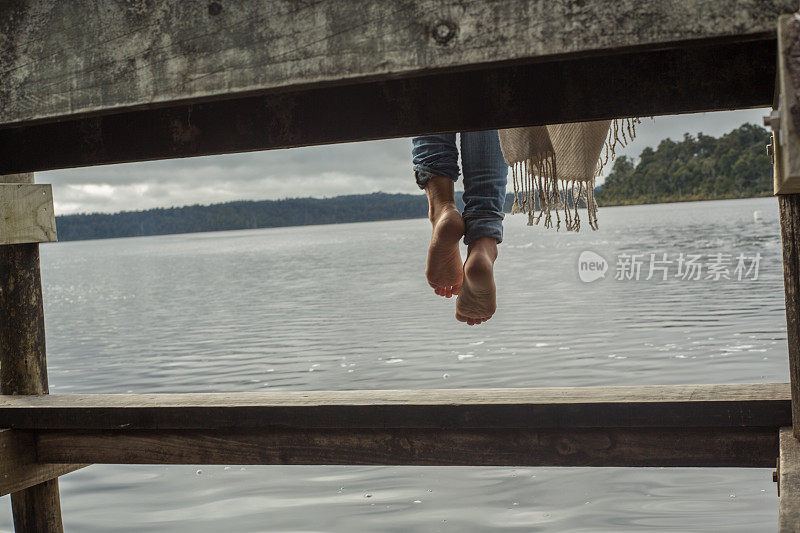 女人的双脚悬在湖面上的木制码头上