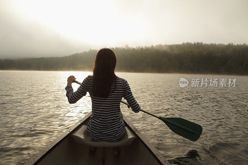一个年轻的女孩在雾蒙蒙的湖面上划着独木舟