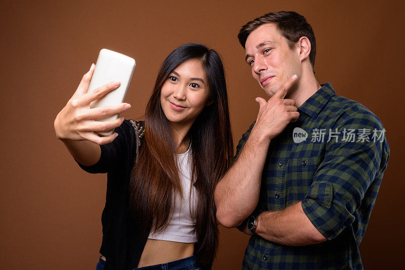 工作室拍摄的年轻英俊的男子和年轻美丽的亚洲女子一起使用手机以彩色背景