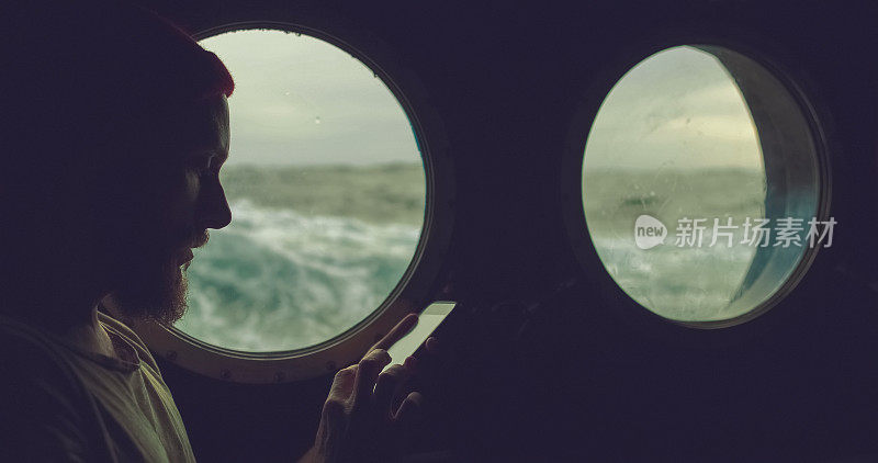 在波涛汹涌的海面上，一个人在一艘船的舷窗旁