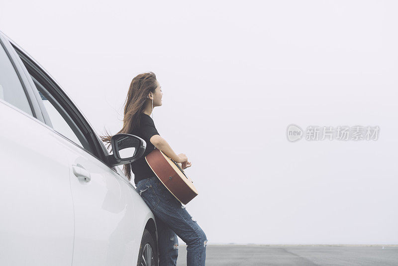 美丽的女孩听着音乐，靠在汽车引擎盖上弹吉他