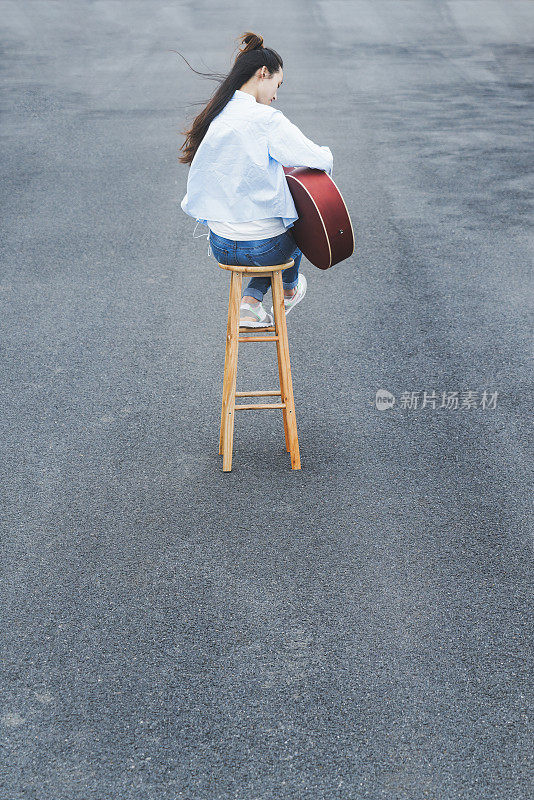 年轻女子坐在凳子上弹吉他