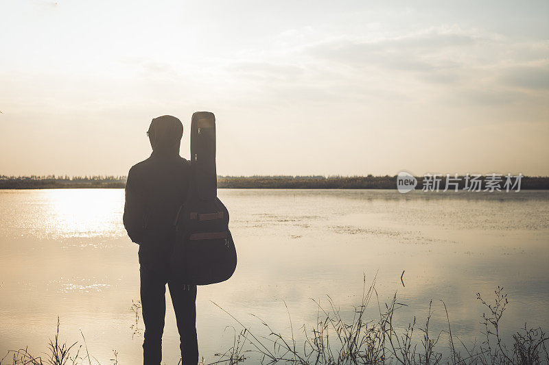 年轻男子拿着吉他站在河边