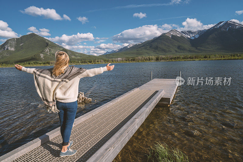 年轻女子在湖边的码头上张开双臂