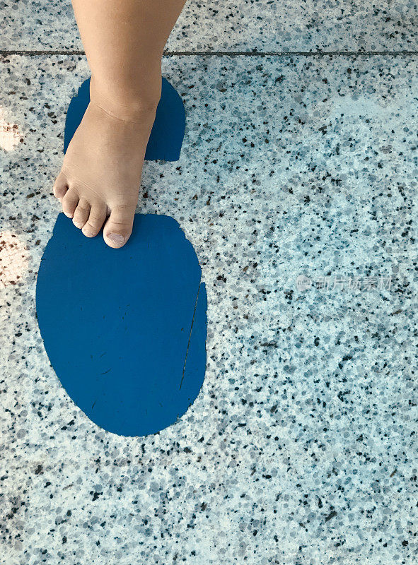 蹒跚学步的孩子的脚踩在蓝色的鞋子上，巨大的脚步踩在花岗岩上