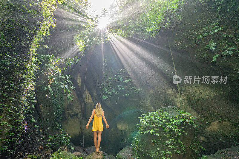 在巴厘岛的热带雨林中，旅行的年轻女子张开双臂拥抱大自然的美丽。人们以自然为旅游理念。