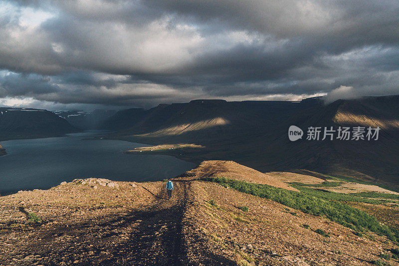 穿着蓝色雨衣的女人一边看峡湾的风景一边散步