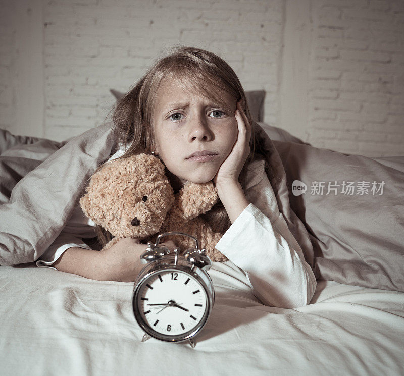 可爱的失眠小女孩躺在床上显示闹钟看起来很累，有睡眠问题，晚上睡不着或醒得太早在儿童失眠，焦虑和睡眠障碍。