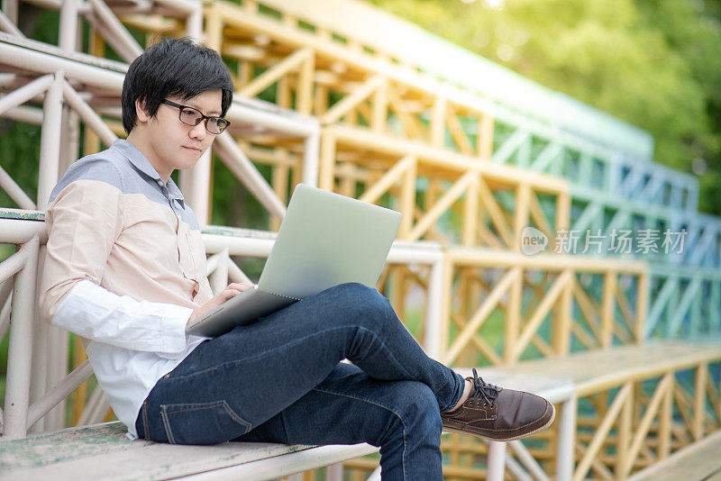 年轻的亚洲男子大学学生使用笔记本电脑站在学院欢呼。校园生活与科技。教育机会或奖学金概念