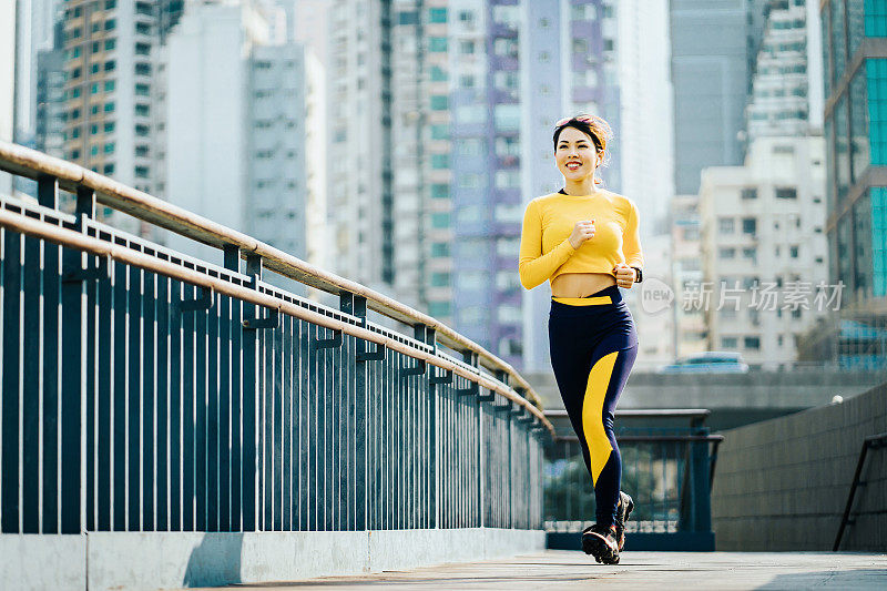 自信和精力充沛的亚洲运动女人在城市桥户外对城市城市天际线慢跑