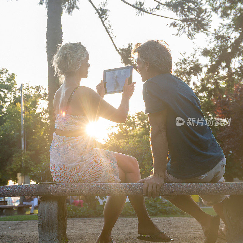 一对成熟的夫妇坐在公园里，在日出时使用数码平板电脑