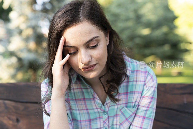 一个沮丧的女人双手捂着头。她坐在花园里。概念抑郁和悲伤。