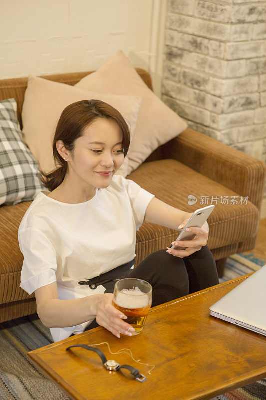 中年女性在客厅用智能手机喝啤酒