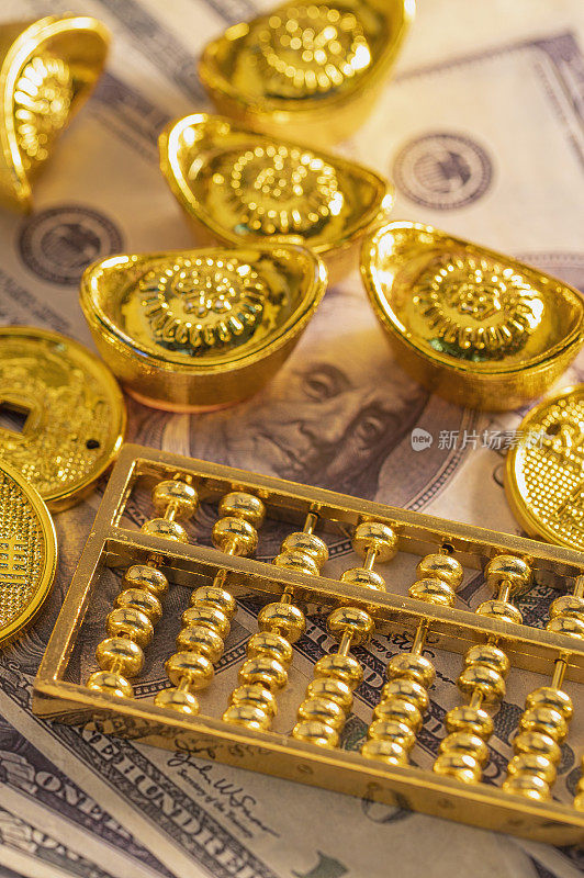 美金纸钞上面放着元宝金币和算盘