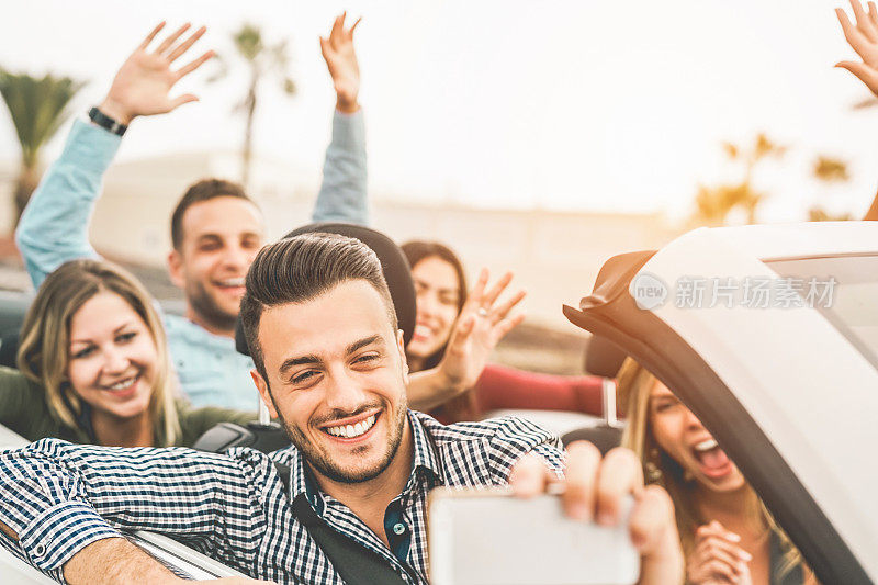 快乐的朋友在敞篷车自拍用手机的相机-年轻人在他们的公路旅行度假cabriolet汽车的乐趣-旅游和青年的生活方式概念