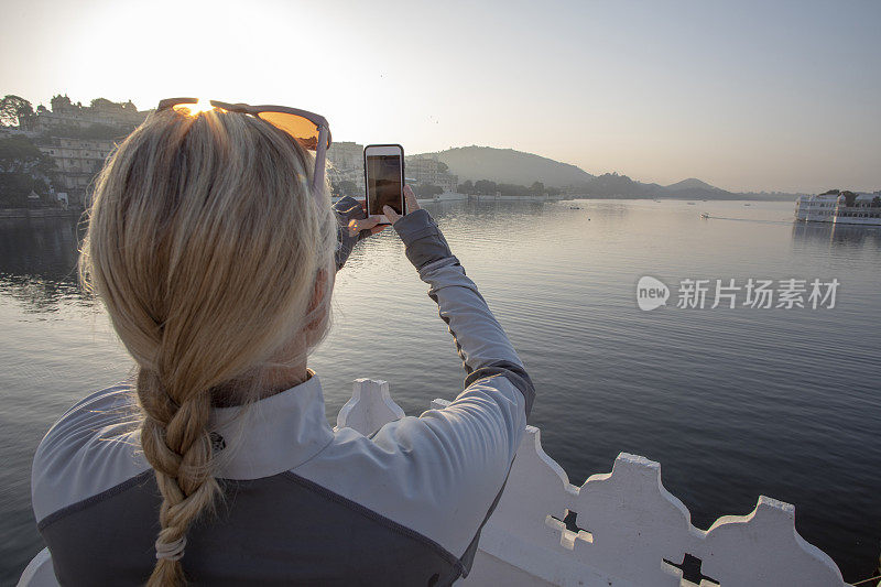 成熟的女人拿着手机拍照，望向湖面