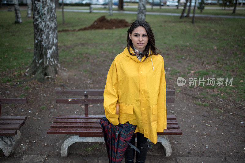 穿着黄色雨衣的年轻女子在公园里度过雨天