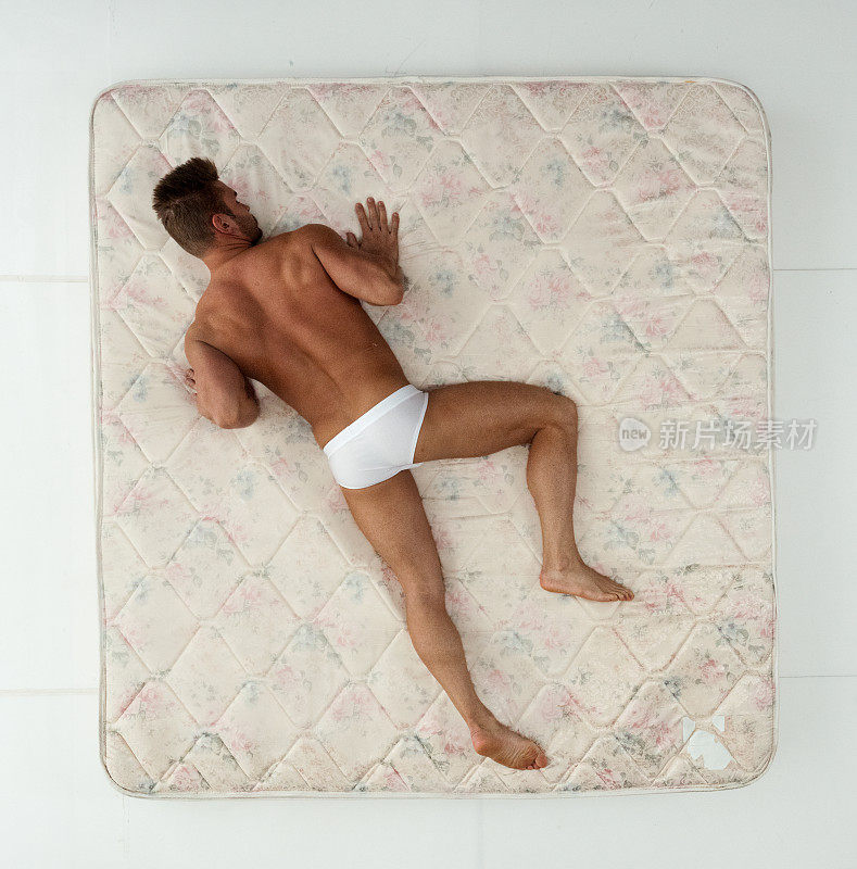 一名男性穿着内衣躺在卧室的白色背景前