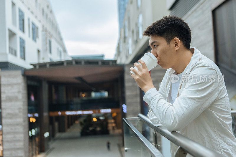 一个阴天，一位男商人正在公司外的阳台上休息咖啡休息——下班后喝一杯咖啡，促进健康，工作生活平衡