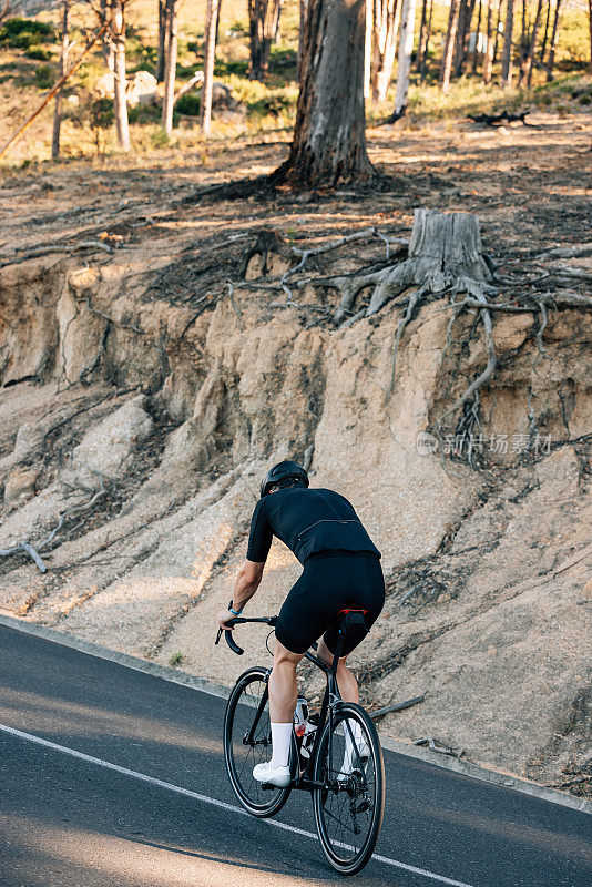 一名身穿黑色运动服的男子骑着自行车在乡间小路上爬山的后景