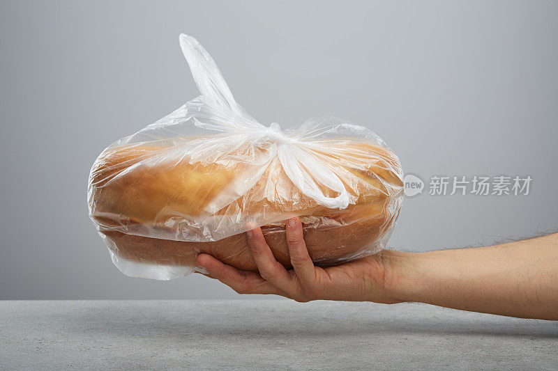 手拿着一个装在塑料袋里的面包放在桌子上