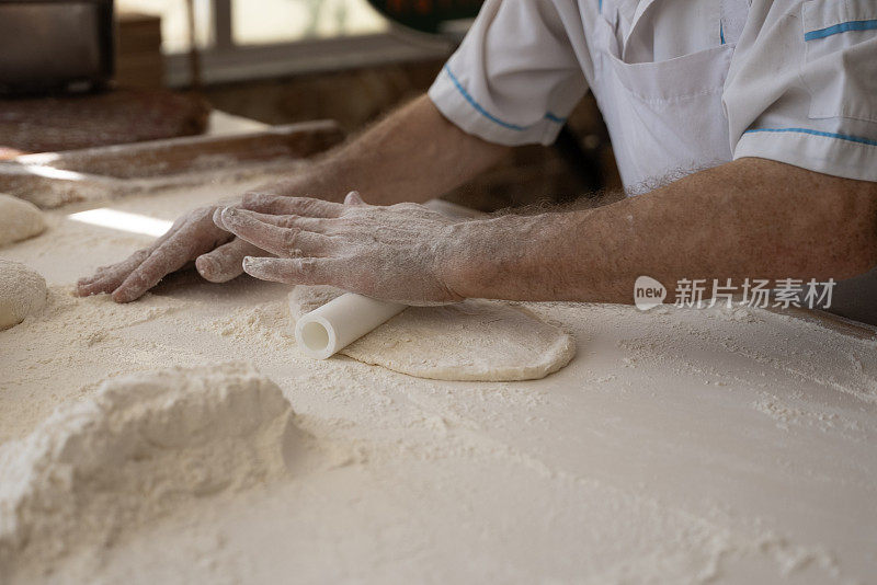 一个老人在面包店做面包，把面团铺好