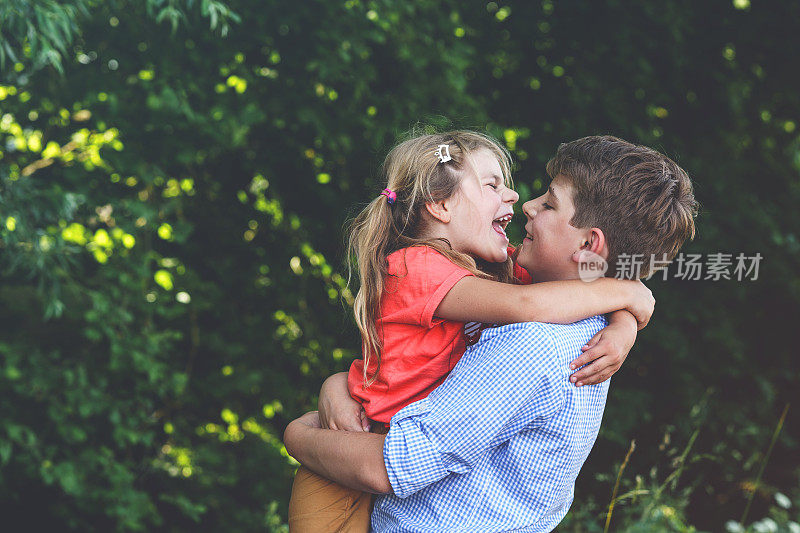 快乐的小女孩拥抱她可爱的弟弟，十几岁的男孩，展示了他们家庭关系中的温暖和爱。无忧无虑的童年，兄妹情谊。