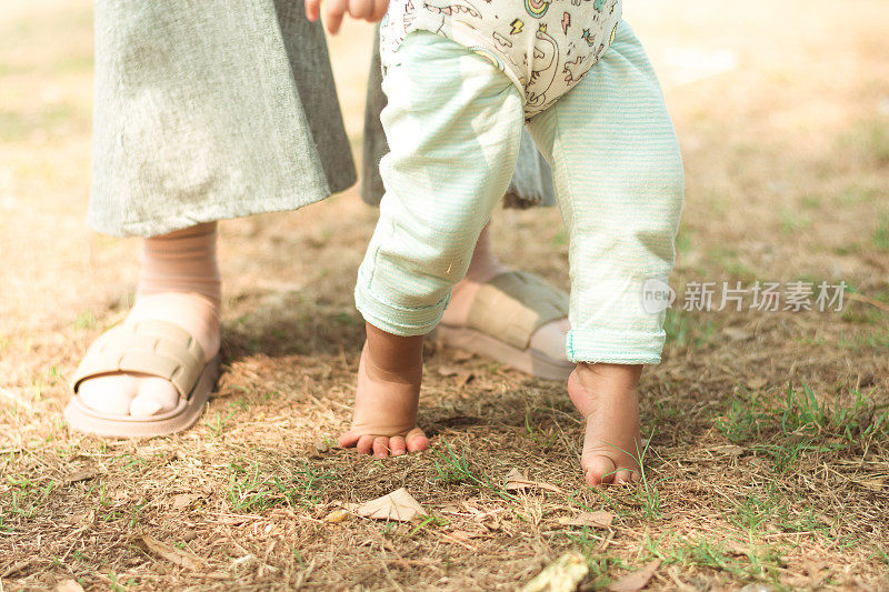 的第一步。宝宝的脚在地上走路的特写，她的妈妈小心地扶着她
