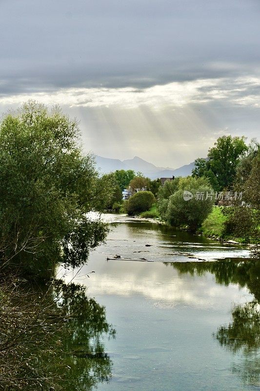 一缕缕光线从云层中冲出，落在河上。来自云的光线。阳光穿透云层，指向水面。初秋的巴伐利亚风景。河流、树木和阳光透过云层。