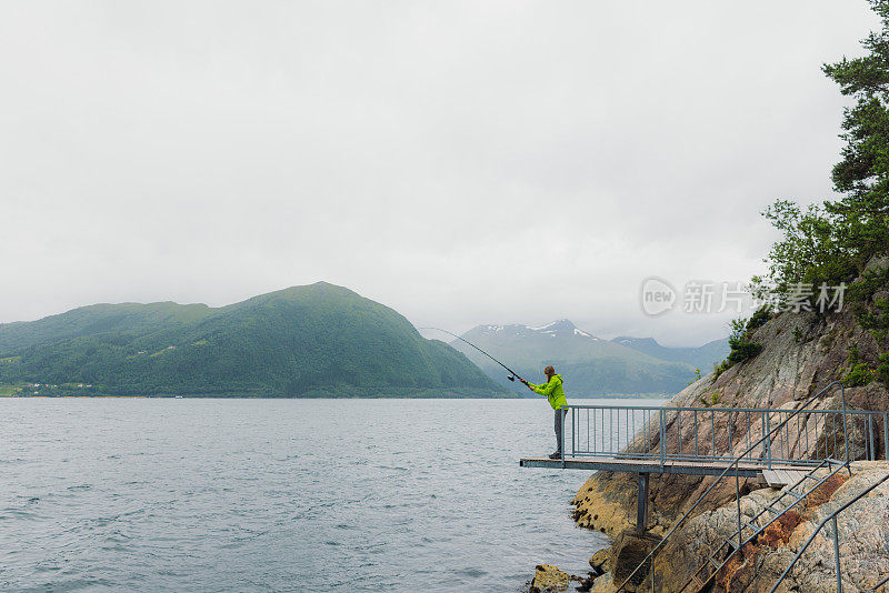 身穿绿夹克的女子在挪威峡湾钓鱼