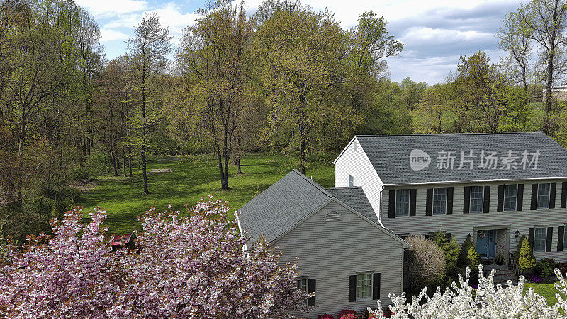 新泽西春天林地里的房子。在阳光明媚的春天，一栋两层楼的房子和绿色草坪上盛开的五颜六色的树木