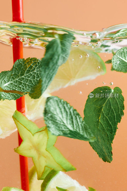 将柠檬片和杨桃片与薄荷叶一起浸泡在红色吸管的水中。清爽的柠檬水。质地清凉甜美的夏日饮品。